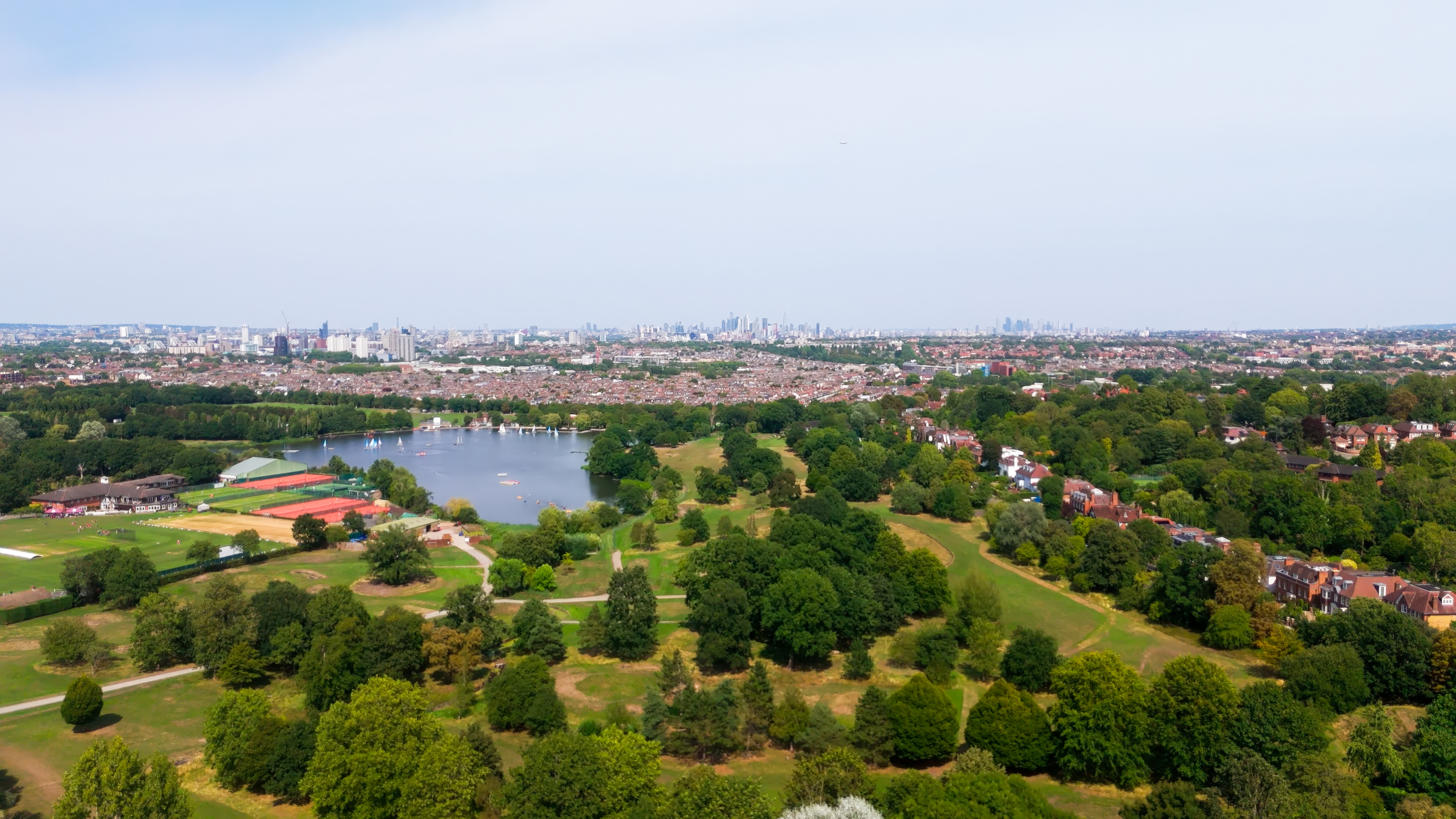 Aerial view across Wimbledon Park, showing the lake, open green space and the London skyline beyond.